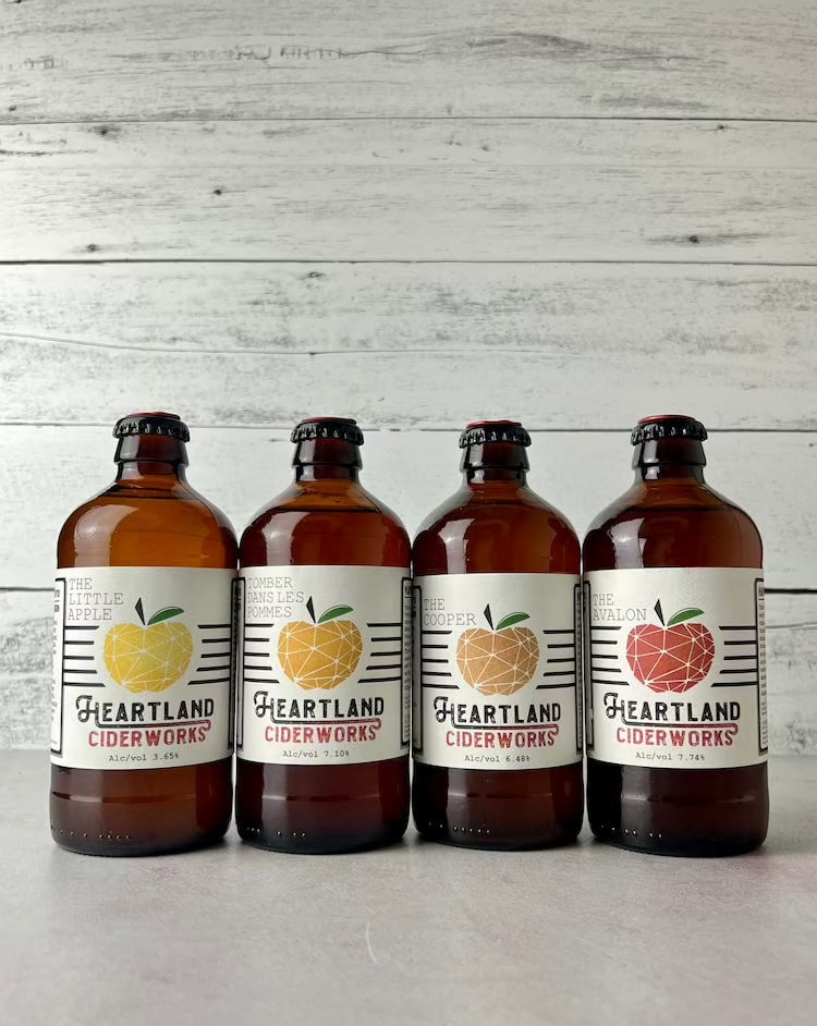 Four 12-oz bottles of Heartland Ciderworks cider: The Little Apple, Tomber Dans Les Pommes, The Cooper, The Avalon
