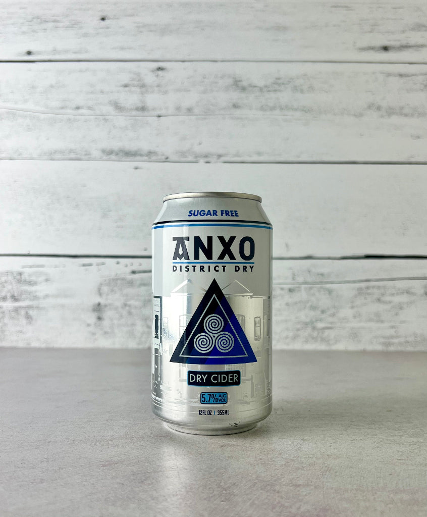 Photo of a 12-oz can of Anxo District Dry cider on a gray surface with a white wooden background