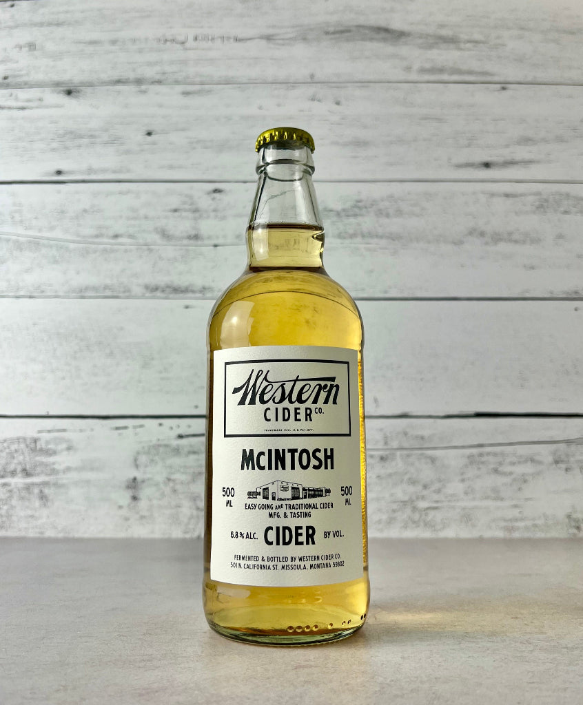 photo of a 500 mL Bottle of Western Cider McIntosh cider on a wooden surface with a light gray background