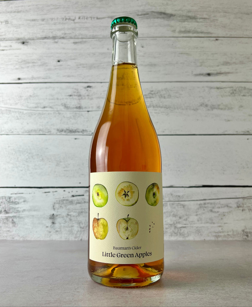 750 mL Bottle of Bauman's Cider Little Green Apples cider on a white wooden backdrop