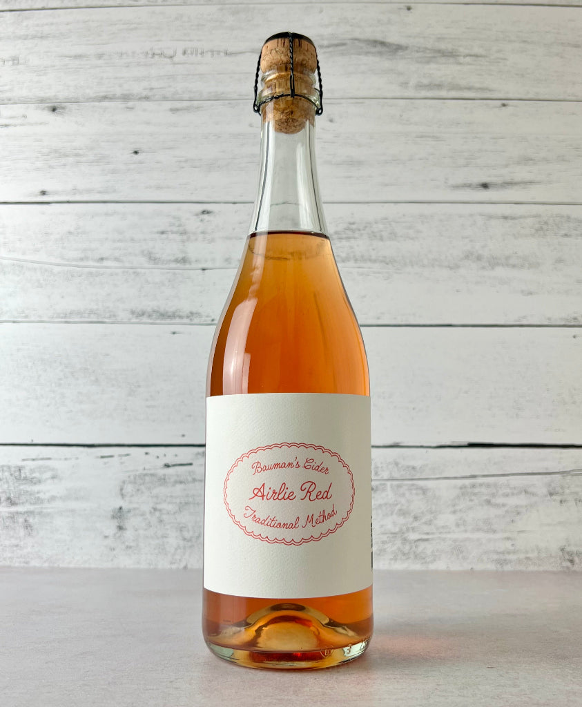 Photo of a 750 mL Bottle of Bauman's Cider Airlie Red Traditional Method cider on a wooden surface