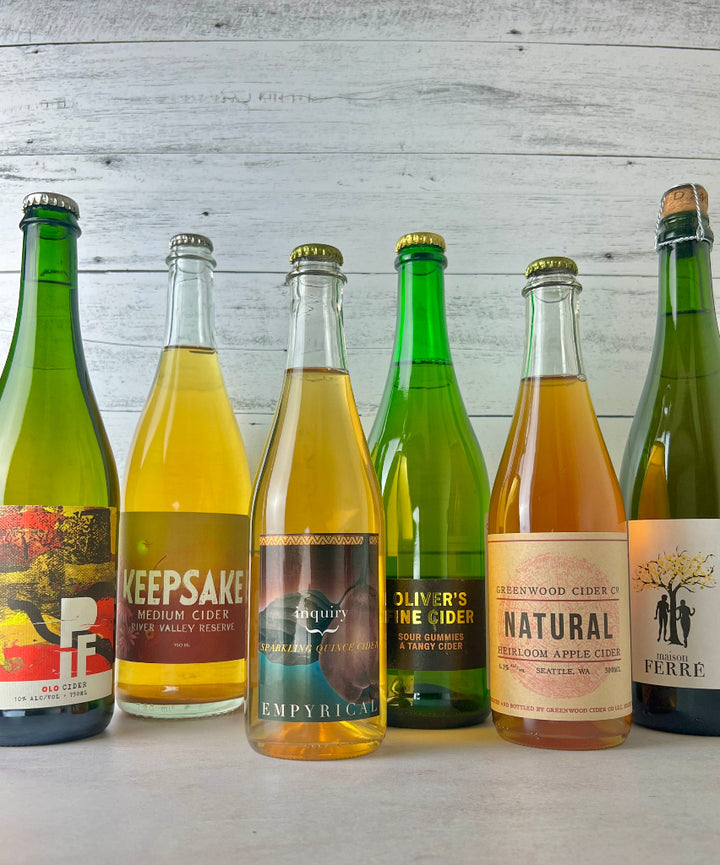 Photo of 6 ciders, from left to right: PIF OLO Cider, Keepsake Medium Cider River Valley Reserve, Empyrical Inquiry Quince Cider, Oliver's Fine Cider Sour Gummies, Greenwood Cider Natural Heirloom Cider, and Maison Ferre