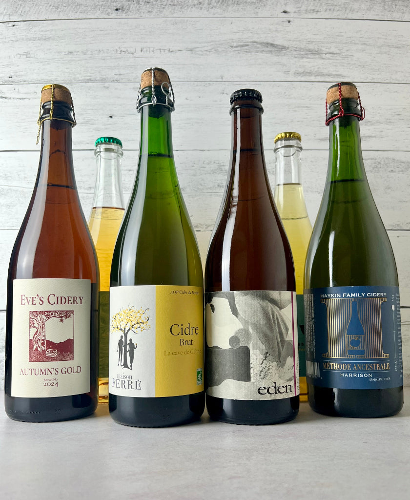 Photo of six 750 mL bottles of cider, with four labels visible from left to right: Eve's Cidery Autumn's Gold, Maison Ferre Cidre Brut, Eden Cider, Haykin Family Cidery Methode Ancestrale Harrison