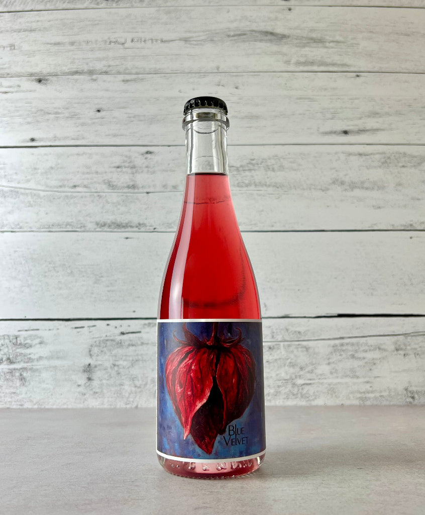 Photo of a 375 mL bottle of Botanist & Barrel Blue Velvet Cider. Bright pink cider in a clear bottle.