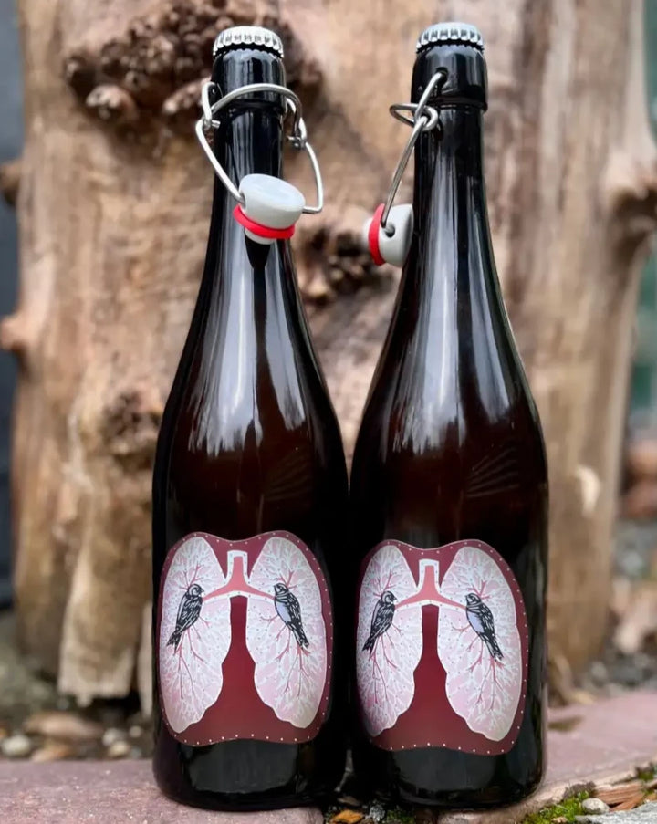 Two bottles of Art & Science Symbiosis Cider. Label art is of a pair of lungs with two birds