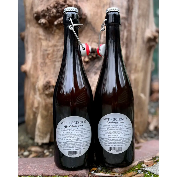 Two bottles of Art & Science Symbiosis cider showing the back labels. One label says 2019 and the other says 2020.