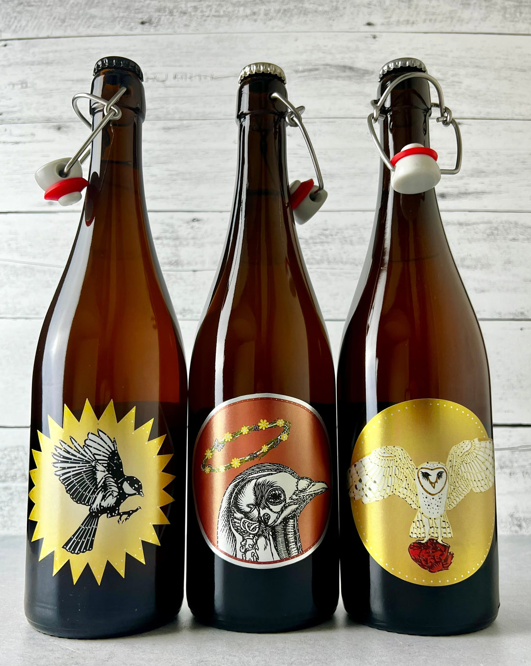 Three 750 mL bottles of Art + Science cider, depicting bird art on the labels - Clutch Cider, Birdbrain Perry, and Quince