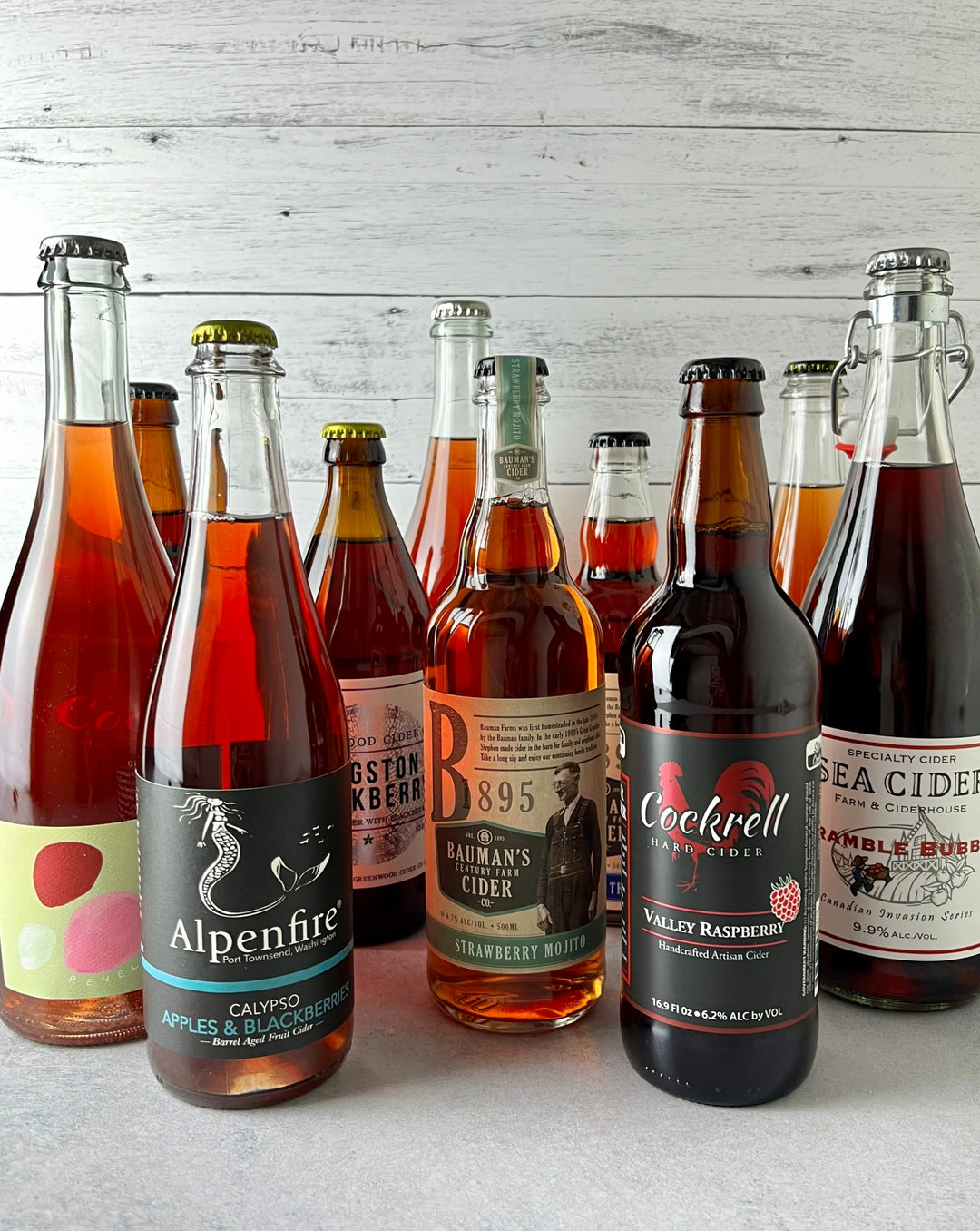 Multiple bottles of fruited cider, including Revel, Alpenfire, Bauman's, Cockrell, Sea Cider, and Greenwood 