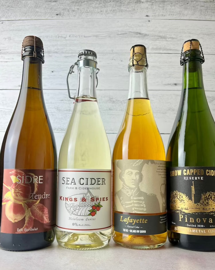 Four 750 mL bottles of cider, from left to right: Eric Bordelet Sidre Tendre, Sea Cider Kings & Spies, Liberty Lafayette Keeved, Snow Capped Pinova 