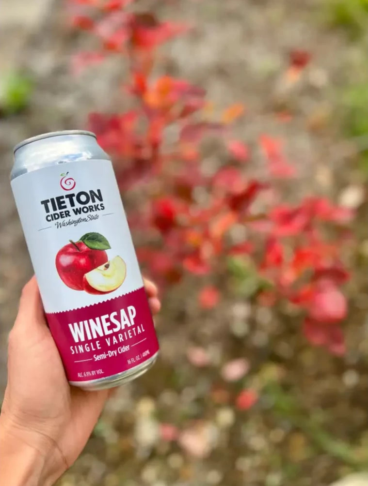 hand holding a 16 oz can of Tieton Cider Works Winesap Single Varietal Cider, with fall leaves in background
