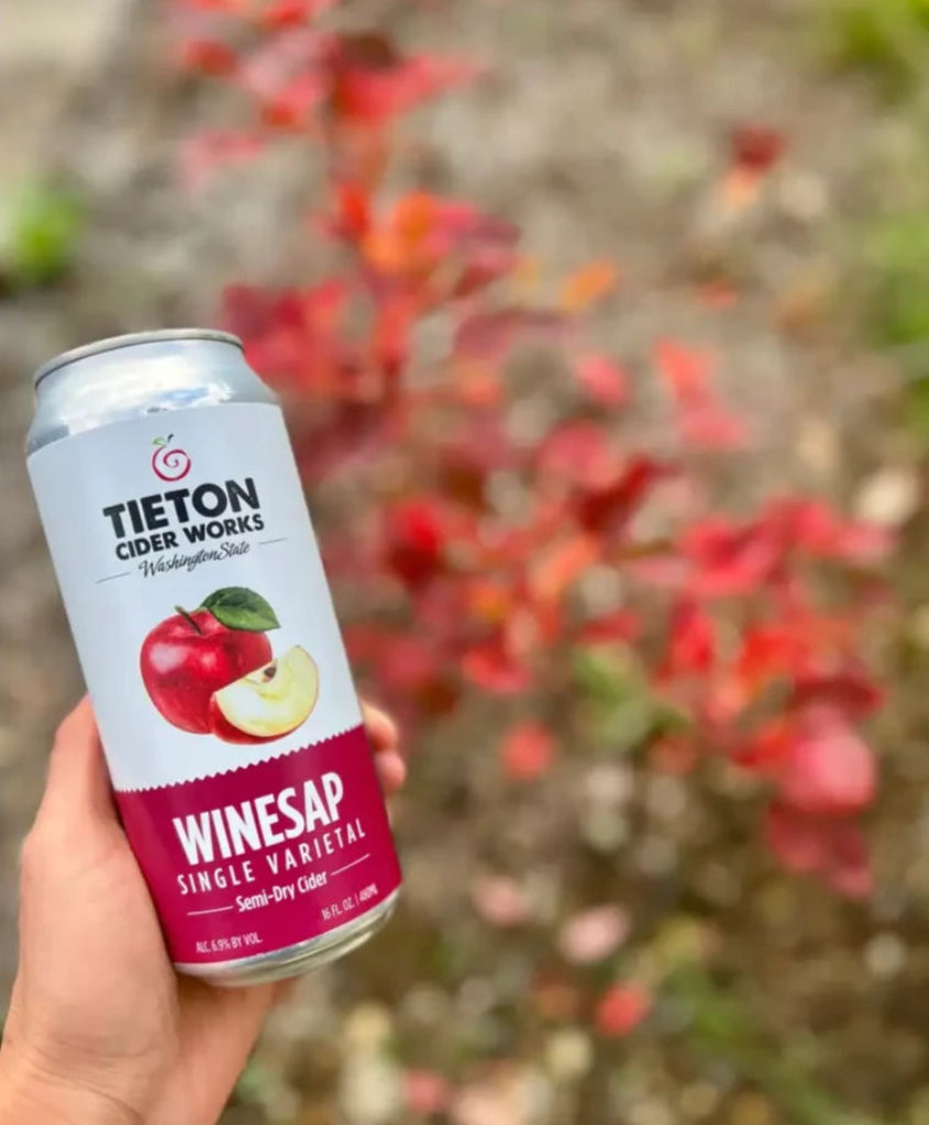 hand holding a 16 oz can of Tieton Cider Works Winesap Single Varietal Cider, with fall leaves in background